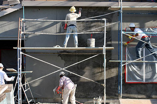 three workers on scaffolding stuccoing a home