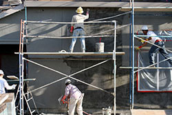  three workers on a scaffold completing hardcoat stucco on home