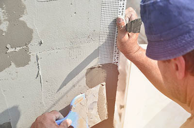 man holding stucco mesh against wall while he applies stucco