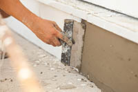 worker completing stucco repair under a window sill due to water intrusion