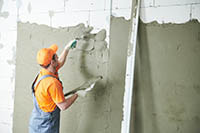 worker holding trowel completing a stucco installation on large wall