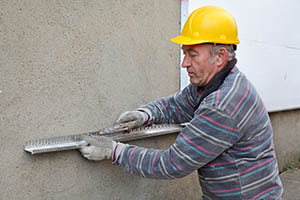 worker leveling stucco on the exterior of a home after patching